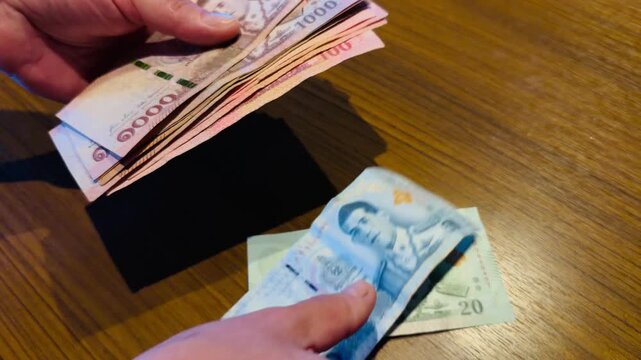 Hands counting Thai Baht banknotes over a wooden table. Close-up of 1000, 100, 50, and 20 THB bills. Concept of travel budget, currency exchange, and financial transactions in Thailand.