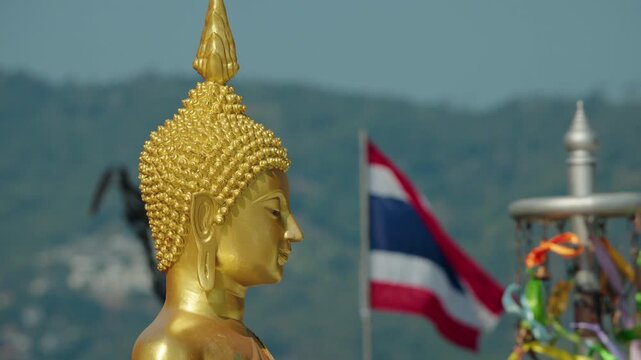 Golden Buddha statue close up with Thai flag in background, sacred Buddhist symbol on mountain viewpoint with serene spiritual atmosphere in Thailand