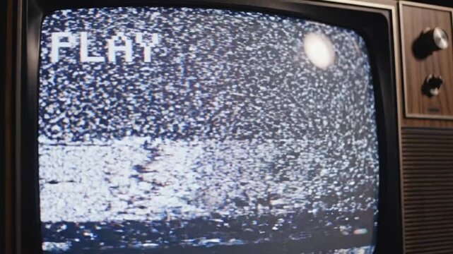 Old damaged VHS tape plays with noise on a vintage television set from the 1980s in a dimly lit room