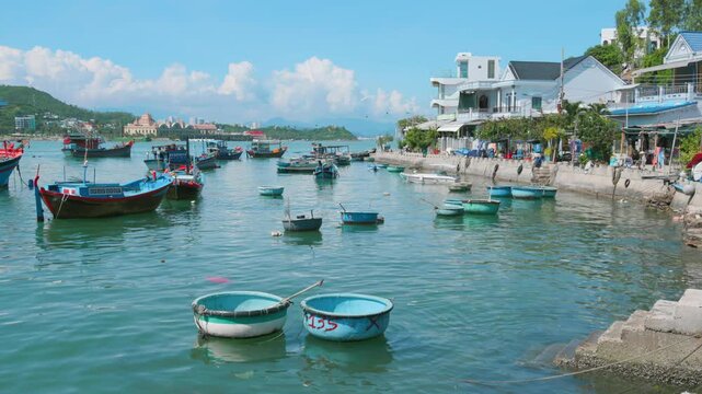 A scenic view of traditional Vietnamese coracle boats and fishing vessels moored in the turquoise waters of Hon Meiu Island, Nha Trang, Vietnam, with coastal buildings in the background.