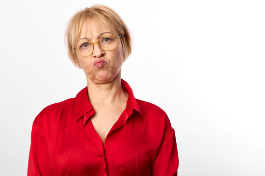 Funny woman with short blond hair and eyeglasses, red shirt on white background, puckered lips expression, playful isolated studio portrait, expressive face, closeup funny mood