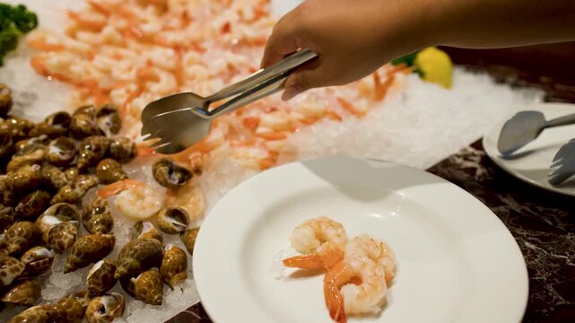 Person Using Tongs to Serve Shrimp and Sea Snails at Buffet