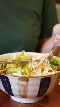 Person Eating Vietnamese Bun Cha Noodles with Chopsticks in Ceramic Bowl