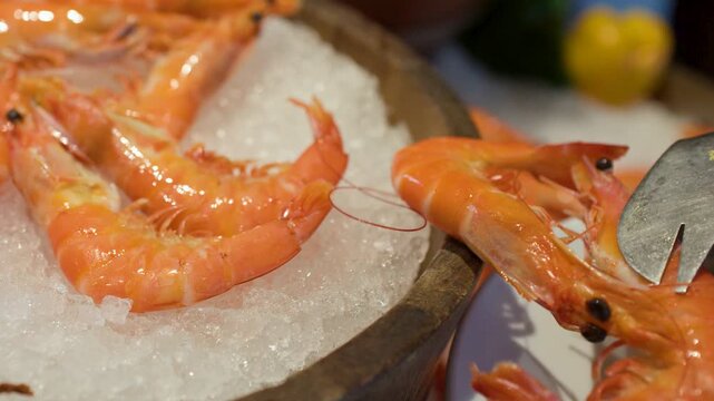 Person Using Tongs to Pick Fresh Cooked Prawns from Ice Buffet