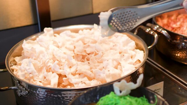 Person Using Metal Tongs to Serve Shrimp Crackers at Buffet