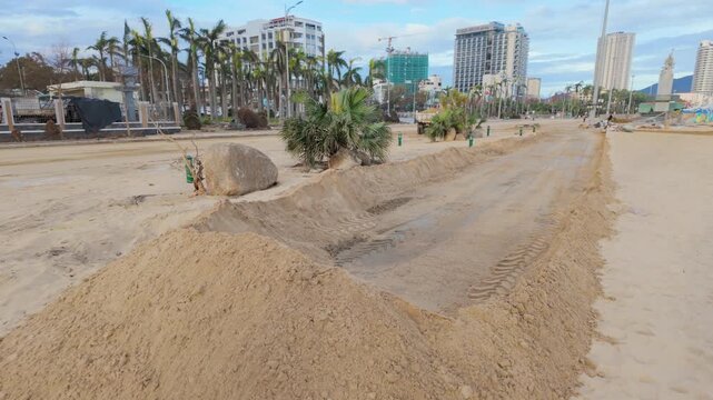 Construction work on a sandy beach in Quy Nhon, Vietnam. Piles of sand and dug trenches indicate ongoing development of the coastal area.