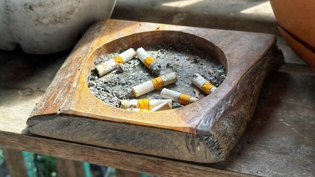 Several cigarette butts are in a wooden ashtray on a table