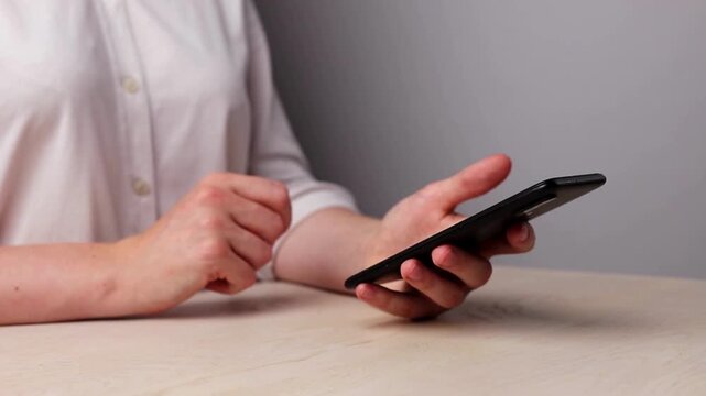 Closeup female relaxes in home using smartphone scrolling on text message or social media internet