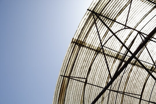 A minimalist composition featuring a curved corrugated roof structure against a clear blue sky. Highlighting rhythmic texture, geometric metal frames, and industrial design utility.