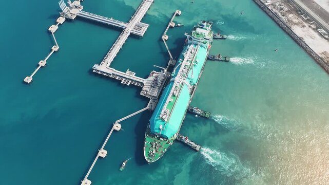 large green LNG tanker ship being assisted by tugboats at a maritime terminal in the Strait of Hormuz. Global energy logistics and international natural gas trade today.