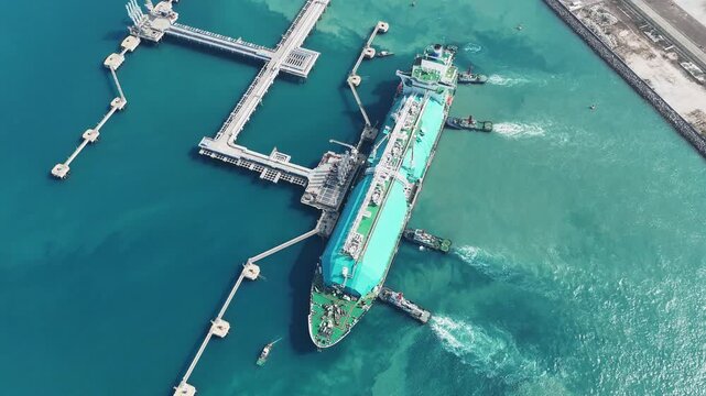 large green LNG tanker ship being assisted by tugboats at a maritime terminal in the Strait of Hormuz. Global energy logistics and international natural gas trade today.