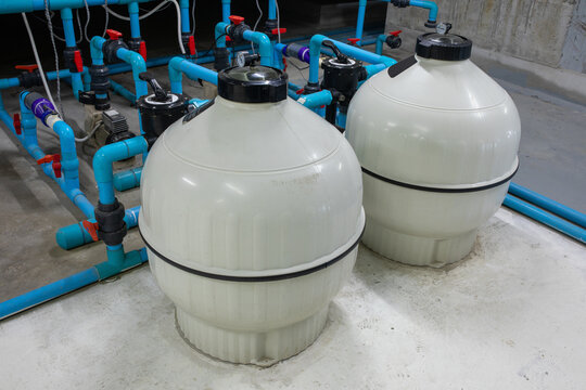 Two white swimming pool sand filter tanks connected to blue PVC pipes and valves in underground pump room