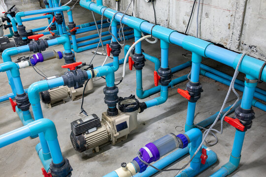 Pool water pump system with multiple blue PVC pipes, ball valves, electric motors and pressure filters in mechanical room of hotel or resort in Asia