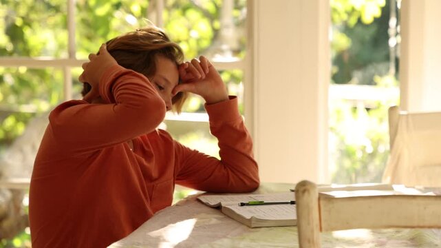 12 year old boy doing homework at kitchen table at sunset