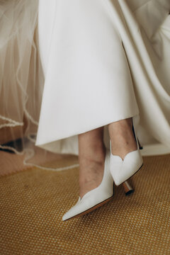 Bride wearing elegant white wedding shoes on carpet
