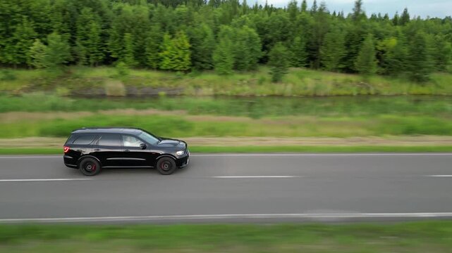 Black luxury SUV driving fast on a scenic highway through green forest landscape