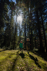 Obraz premium Two children joyfully run hand-in-hand on a mossy forest floor. Sunlight filters through tall trees, creating a magical atmosphere.