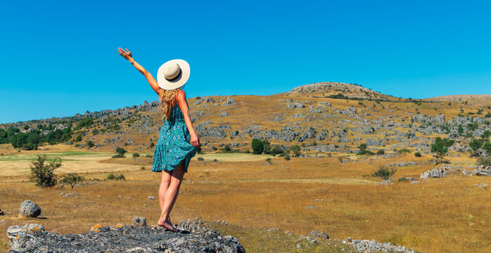 happy woman traveler in summer dress raising hand on top of mountain enjoying nature freedom