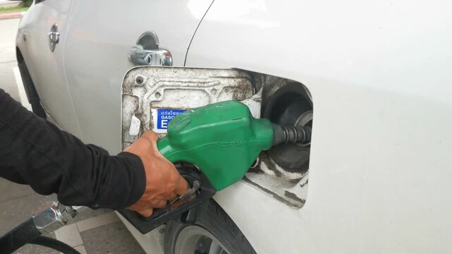 Young man fueling his car at gas station, using the pump nozzle. Late at night inserting a gasoline hose into the auto tank of auto at gas station.