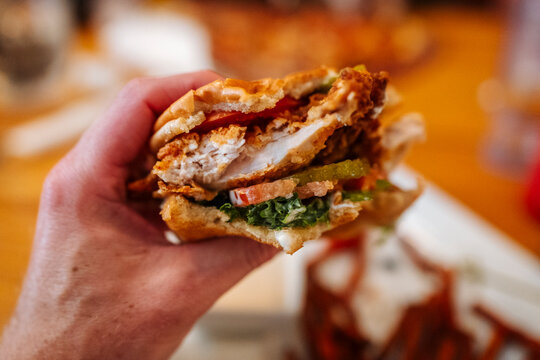 Hand holding bitten chicken sandwich with layered ingredients.