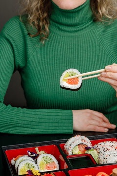Girl eating Asian food from bento box with chopsticks