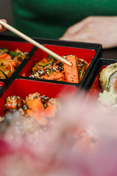 Girl eating Asian food from bento box with chopsticks