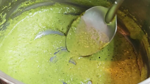 Close-up of stirring fresh Thai green curry paste in a stainless steel pot.