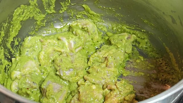 Stir-frying raw chicken with aromatic green curry paste in a stainless steel pot.
