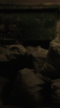 Dark bags filled with refuse sit quietly in a neglected alleyway. Dim lighting casts an eerie ambiance, revealing the aftermath of careless disposal in the heart of the city.