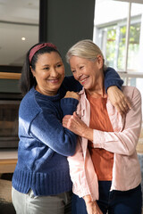 Naklejka premium Mature female friends hugging in living room, wearing blue sweater and pink shirt, ring showing