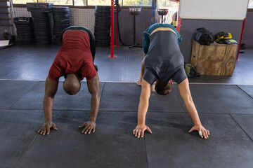 Fototapeta premium Diverse male training partners stretching in gym on rubber tiles near red rig and plyo box