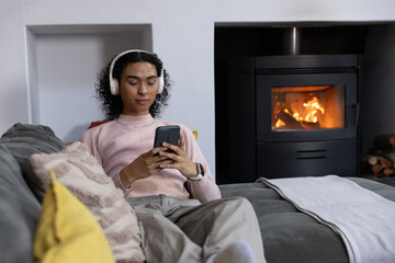 Naklejka premium Nonbinary person reclining on gray sofa in cozy living room, wearing pink sweater and holding phone
