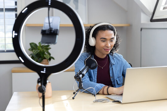 Nonbinary creator sitting at home desk streaming with ring light phone mount, denim jacket, headset