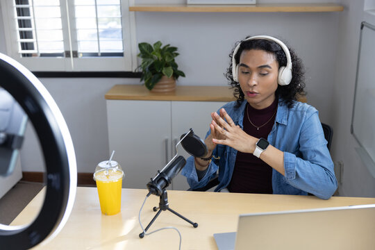 Nonbinary person recording podcast in home studio using microphone, laptop, headphones, copy space