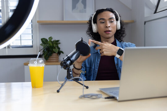 Non-binary adult recording on laptop at home studio desk wearing denim jacket with microphone