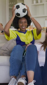 Vertical video: Laughing fan in yellow moving ball on sofa as friend reaching with bottle in match
