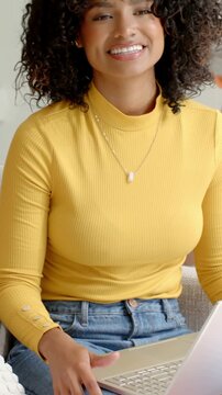 Vertical video: Camera panning woman in mustard top using laptop, laughing with friend on couch