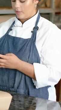 Vertical video: Accepting customer phone, chef in coat and denim apron adjusting box at bakery POS