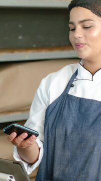 Vertical video: Reacting to blue device, chef in white coat tapping phone at bakery counter smiling