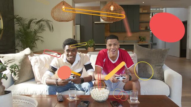 Two men sitting on couch playing game pressing pads causing overlays moving across frame smiling