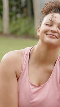Vertical video: Shifting gaze to camera and laughing woman in yard in pink tank top and gold hoops