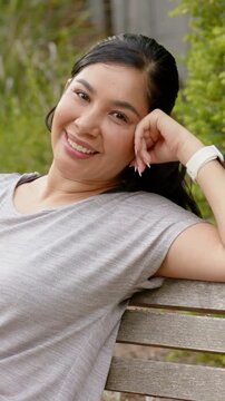 Vertical video: Camera zooming, woman adjusting right hand, relaxing on bench, gray top, smartwatch