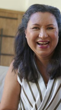 Vertical video: Smiling senior woman reacting to voice, leaning, laughing on sofa, striped top