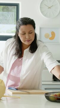 Vertical video: Placing bottle, woman in white top in kitchen picking apple and offering off-screen