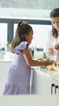 Vertical video: Reaching into yellow bag girl in lavender packing mint box at sink mom giving apple
