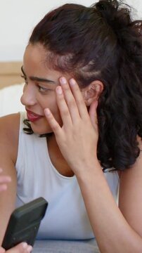 Vertical video: Talking woman being prompted by off-frame voice, reading phone on bed in white top