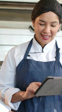 Vertical video: Finishing dough chef in chef coat tapping tablet to confirm recipe at prep counter