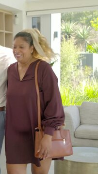 Vertical video: Laughing couple posing at home after man placing arm around woman, holding handbag