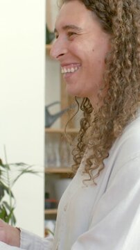 Vertical video: Laughing nonbinary adult in buttonup shirt receiving object at home near plant