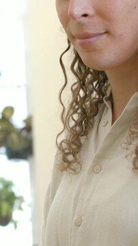 Vertical video: Pulling back camera causing person in beige shirt tending plants at window smiling